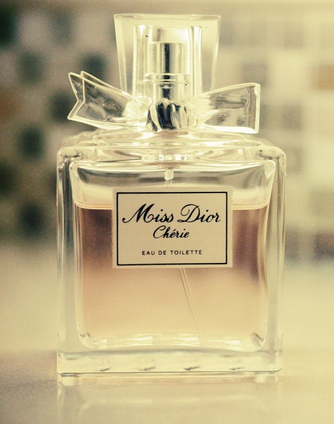 A real bottle of Miss Dior Chérie perfume with pink liquid and a bow
